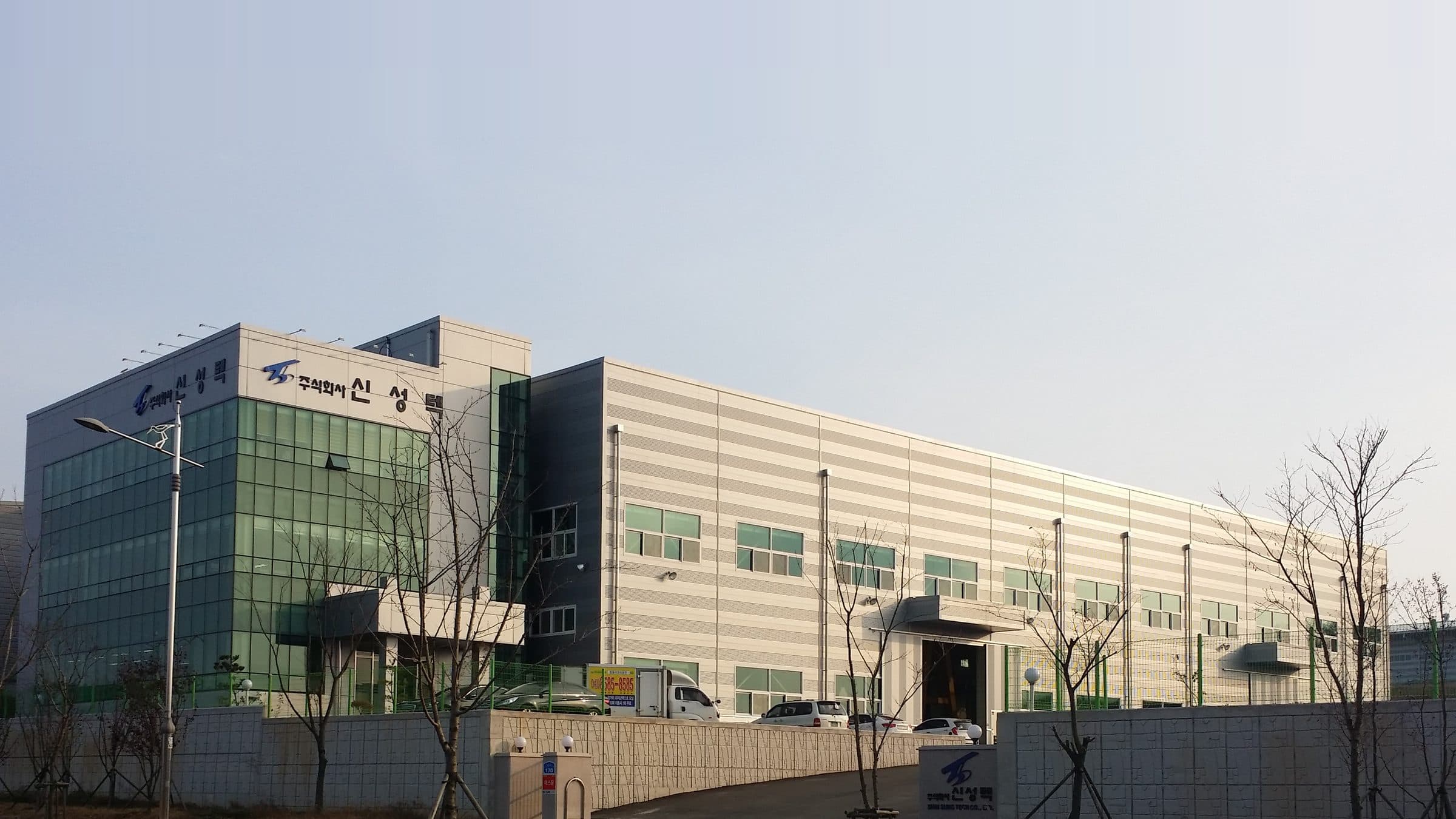 (주)신성텍 서산 성연 공장 전경(2015년 촬영). 왼쪽 유리 사옥 상단에 주식회사 신성텍 사인이 있고 오른쪽으로 생산동이 길게 이어진다.